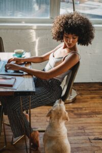 Black woman with fabulous natural hair looks down at her dog while she types on a computer